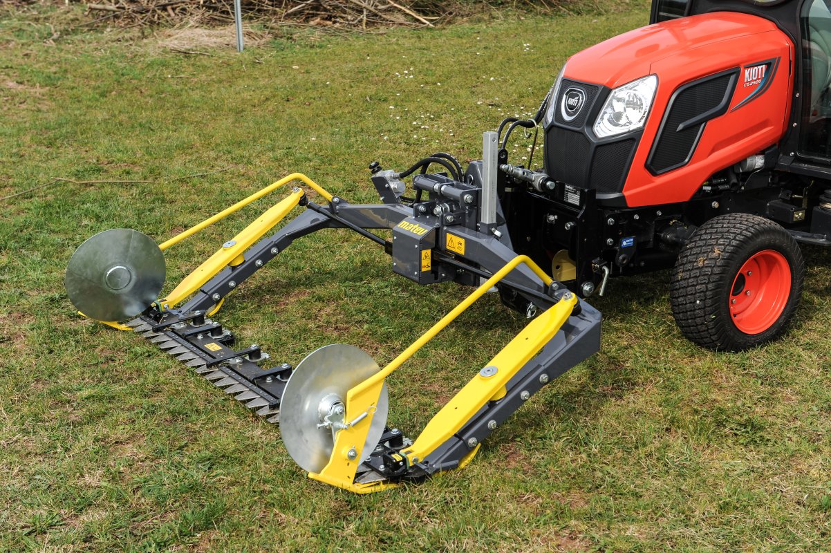 Ein roter Kioti CS2520 Traktor, ausgestattet mit einem matev MOW-PT Portalmähwerk. Das Mähwerk in gelb-grauer Ausführung ist auf einer grünen Wiese abgestellt und zeigt seine robusten Details und präzise Verarbeitung.